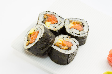Sushi roll in nori on white plate with ginger and wasabi
