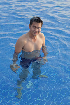 young asian man standing in clear water pool and smiling