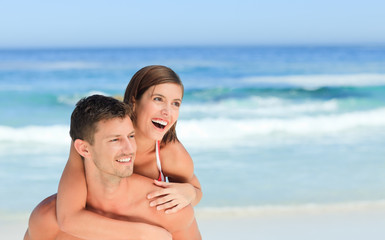 Fototapeta premium Man having wife a piggyback on the beach