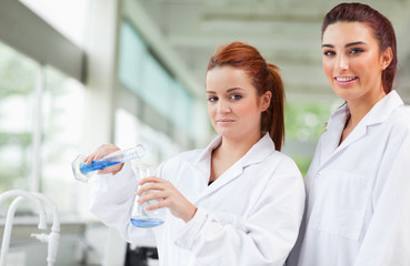 Scientists pouring blue liquid in an Erlenmeyer flask