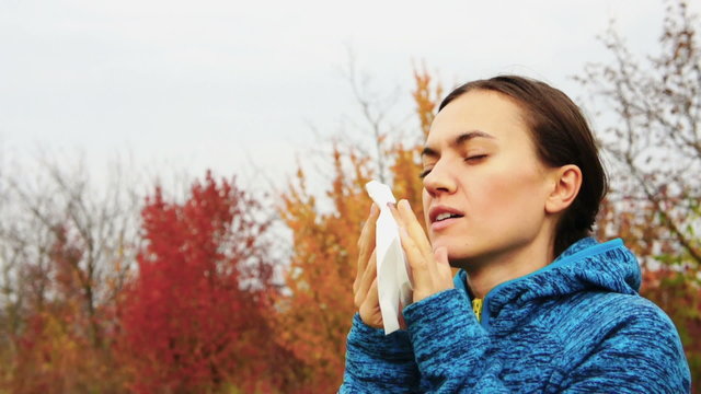 Sick woman blowing her nose into tissue, outdoors