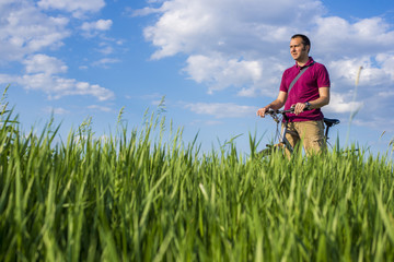Naklejka na ściany i meble Young man standing with bicycle on a green grass