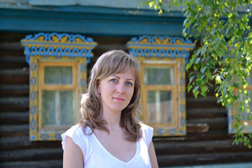Portrait of the young woman against the wooden house with carved