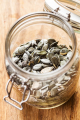 Dry pumpkin seeds in a glass jar, on the brown wooden board