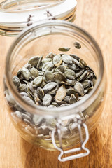 Dry pumpkin seeds in a glass jar, on the brown wooden board