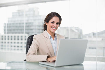 Happy businesswoman typing on laptop at her desk looking at came
