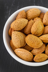 almonds on white bowl on dark background