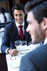 Two smiling business men have dinner at restaurant