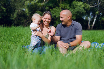 Naklejka na ściany i meble Happy family sitting in a green grass
