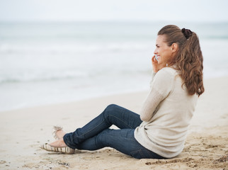 Fototapeta na wymiar Happy womansitting on lonely beach and talking cell phone