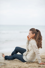 Fototapeta na wymiar Happy young woman sitting on lonely beach and talking cell phone