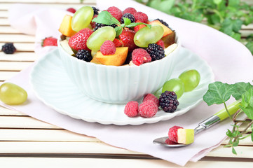 Fruit salad in bowl, on wooden table, on bright background