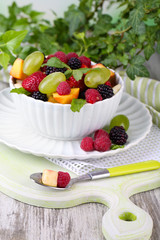 Fruit salad in bowl, on wooden table, on bright background