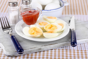 Boiled eggs on plate on wooden board on tablecloth