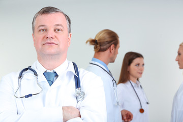 Fototapeta premium Doctor standing in front of coworkers on grey background