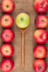 Spoon with green apple lying on the sackcloth among red apples