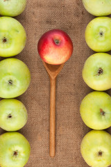 Spoon with red apple lying on the sackcloth among green apples