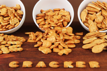 Delicious crackers in bowls on wooden table on brown background