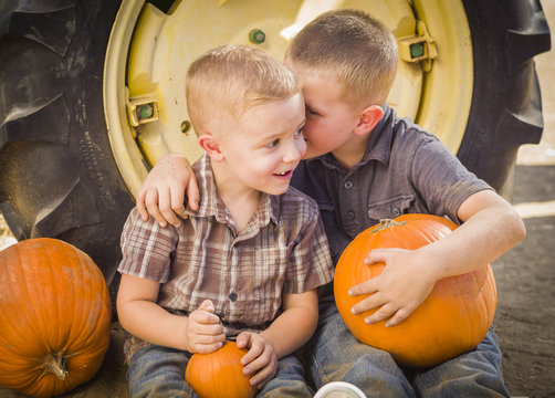 Two Boys Sit Against Tractor Tire Holding Pumpkins Whispering