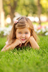 Happy beautiful little girl lying on the grass