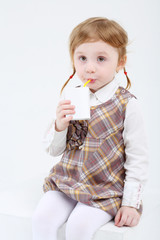 Little cute girl sits and drinks sweet juice on white background