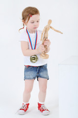 Little girl with medal on chest stands and holds wooden dummy