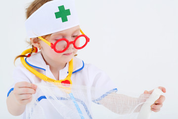 Little girl dressed as nurse spreads bandage on white