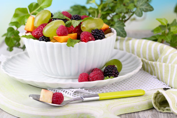 Fruit salad in bowl, on wooden table, on bright background