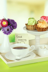 Cup of tea with cakes on wooden tray on table in room