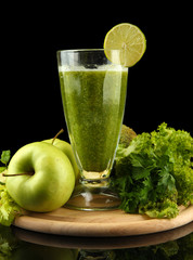 Glass of green vegetable juice and vegetables isolated on black