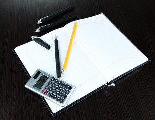 Notebook with pens,pencil and calculator on wooden background