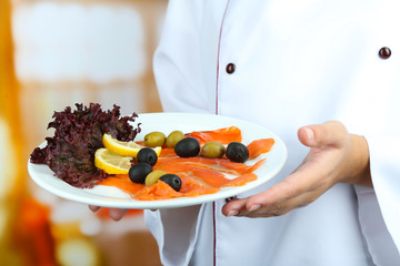 Fish on plate in cook hands on bright background