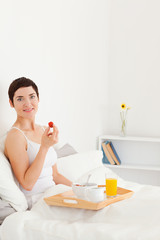 Obraz na płótnie Canvas Portrait of a smiling brunette eating a strawberry