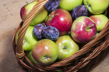 plums and apples in a wicker basket