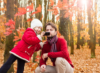 Girl child and father taking autumn photo with mobile phone