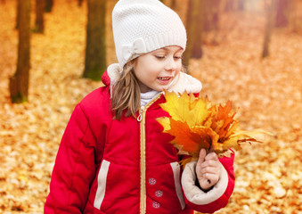 Happy child girl collecting leaves in an autumn park