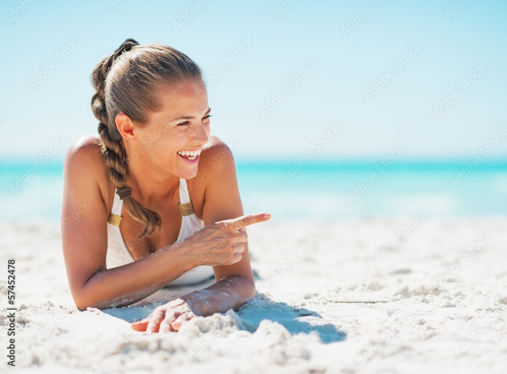 Poster Smiling young woman in swimsuit laying on beach 