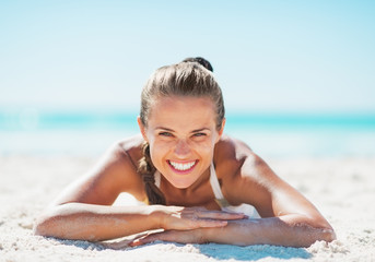 Portrait of smiling woman in swimsuit laying on sandy beach