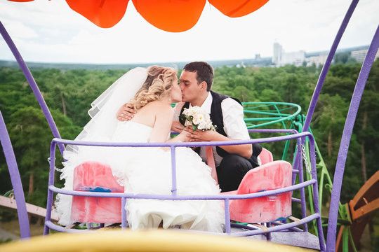 Newly married couple riding on Ferris wheel and kissing