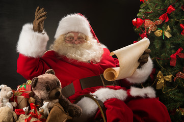 Portrait of happy Santa Claus reading Christmas letter or wish l