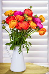 Flowers in a vase with sun light coming out of window blinds