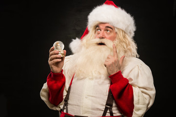Santa Claus holding snow globe against dark background
