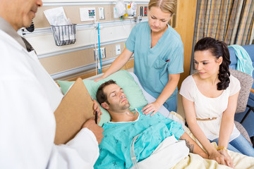 Woman Holding Patient's Hand While Doctor And Nurse Examining Hi
