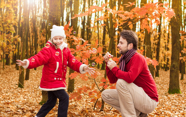 Father and daughter blowing bubbles outdoor in an autumn park