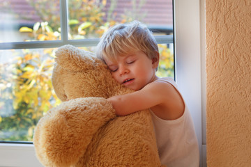 Lovely boy of two years sitting near window with big toy bear.