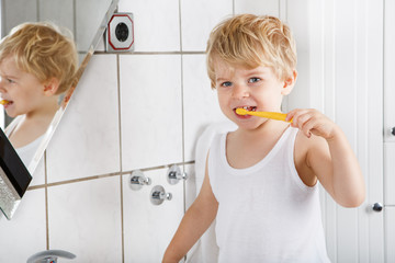 Cute toddler with blue eyes and blond hair brushing his teeth