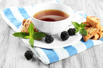 Cup of tea with cookies and blackberry on table close-up