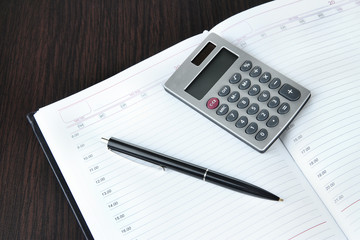 Notebook with pen and calculator on wooden background