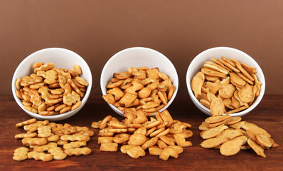 Delicious crackers in bowls on wooden table on brown background