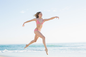 Fototapeta na wymiar Pretty blonde woman jumping on the beach